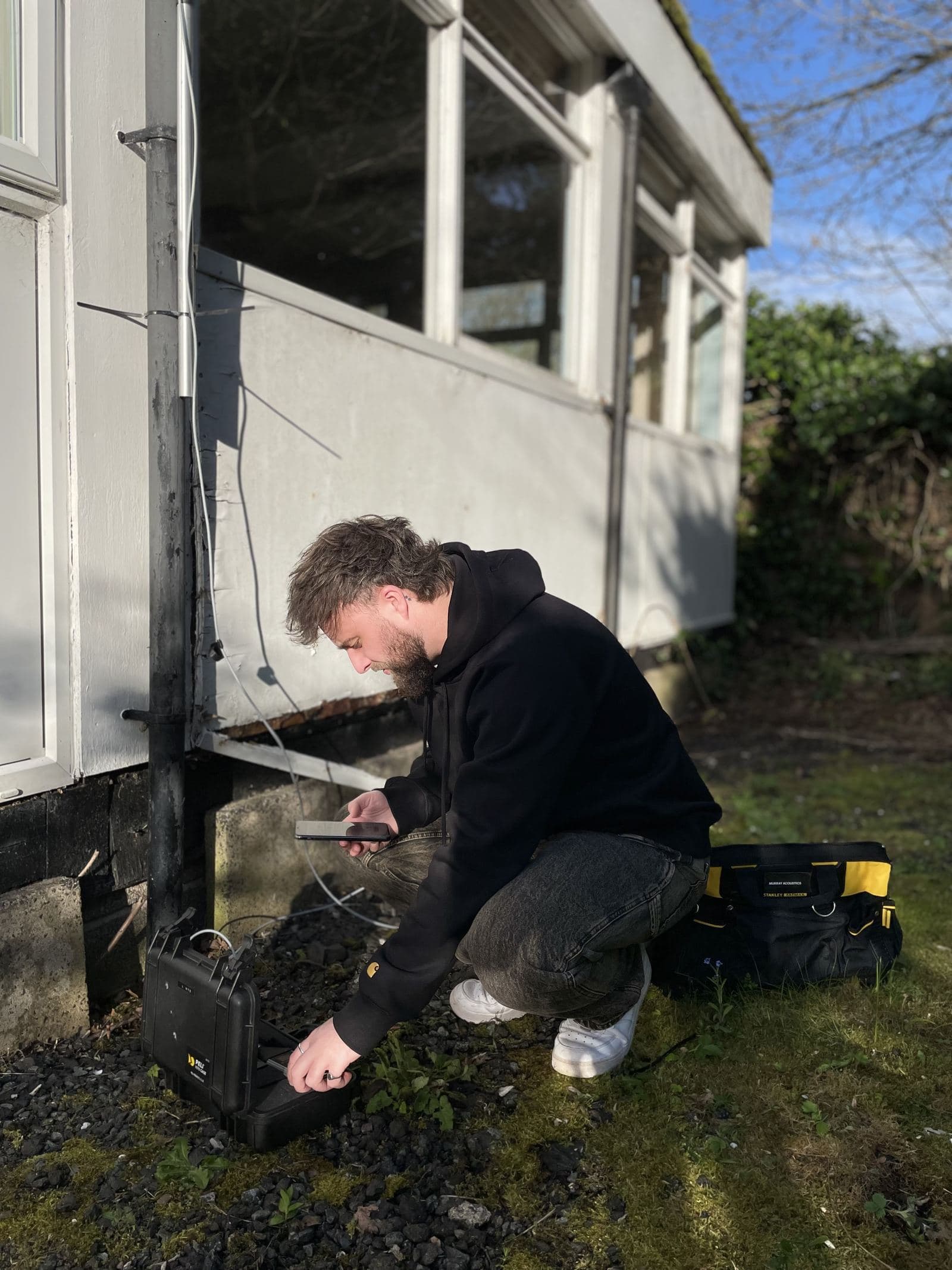 A Murray Acoustics engineer setting up monitoring equipment against a building facade